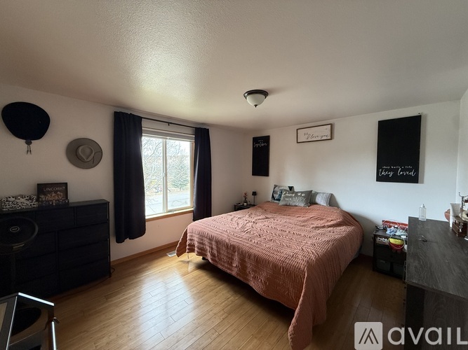 A bedroom with a pink bedspread and a black dresser.