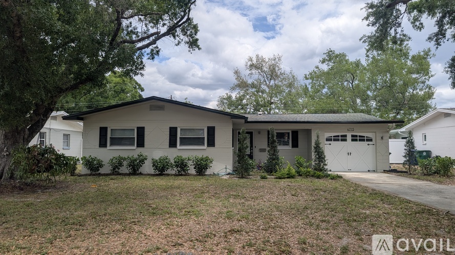 A house with a white exterior and a grey roof is surrounded by greenery.