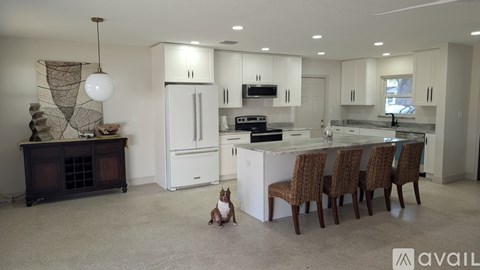 A dog sits in the middle of a modern kitchen with a dining table and chairs.