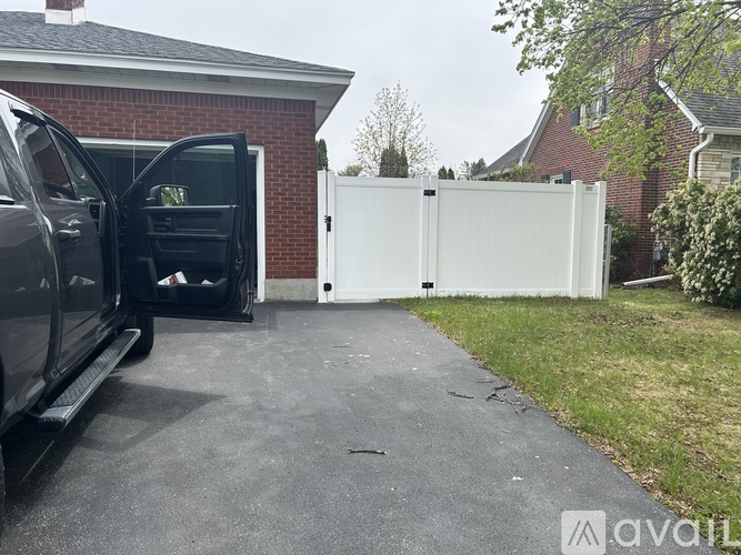 A black car is parked in a driveway with its trunk open.