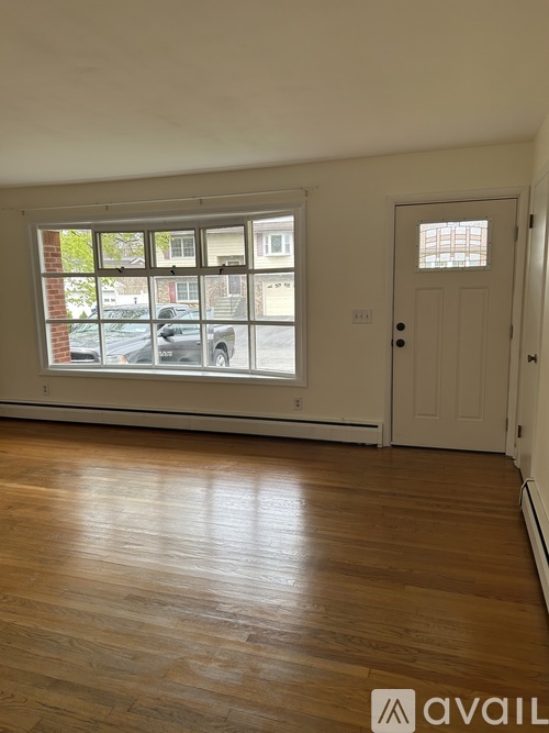 A room with wooden floors and a window showing a parking lot outside.