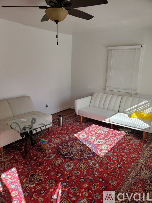 A living room with a rug, a sofa, a table and a fan.