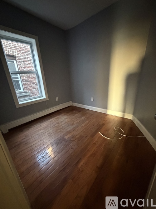 A room with wooden flooring and a window showing a brick building outside.