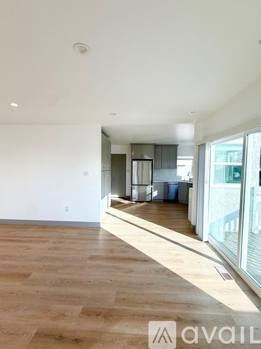 A room with wooden flooring and a view of a kitchen area.