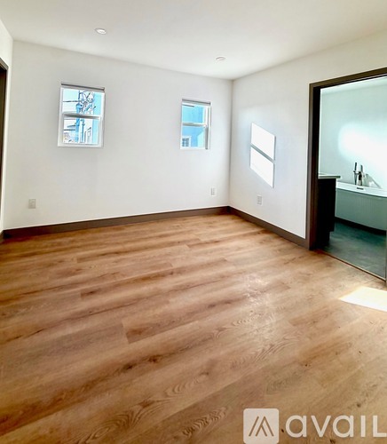A room with wooden flooring and two windows.