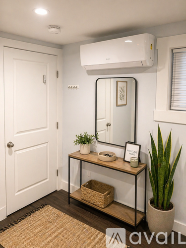 A bathroom with a white door, a mirror, a plant, and a basket on a table.