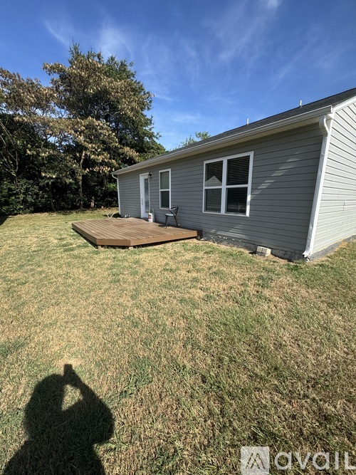 A house with a grey siding and a white door is surrounded by a grassy area.