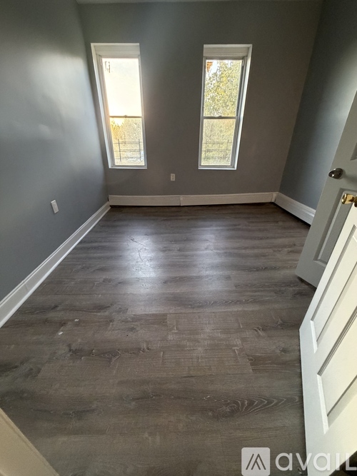 A room with wooden flooring and two windows.