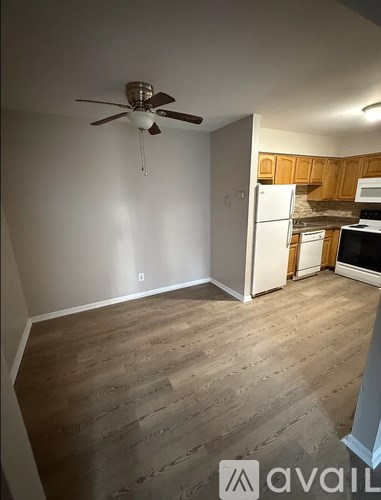 A room with a ceiling fan and a kitchen area in the background.