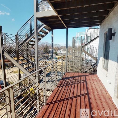 A wooden deck with a metal railing and stairs leading to a building.