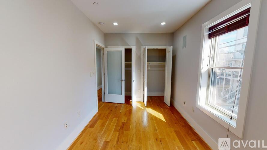 A room with wooden floors and white walls, with two open doors leading to another room.