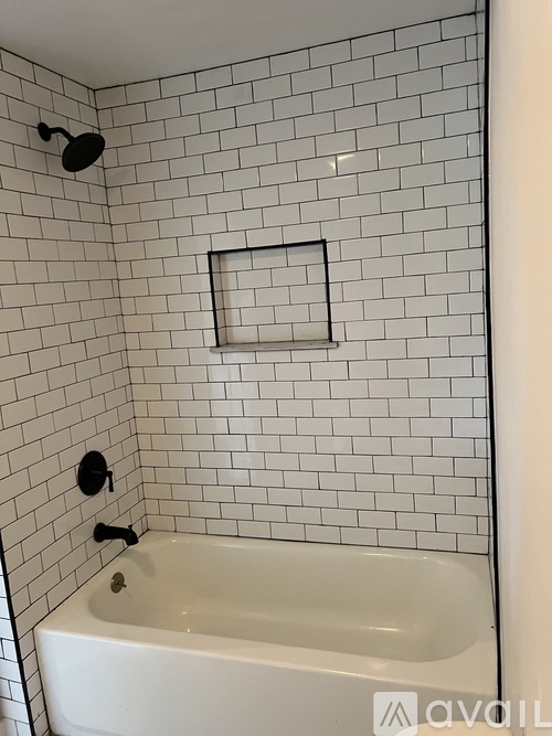 A white bathtub in a bathroom with black fixtures and white tiled walls.