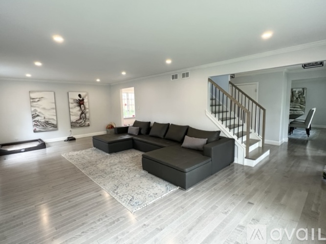 A spacious living room with a grey sofa and a wooden staircase.