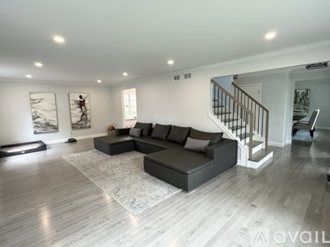 A spacious living room with a grey sofa and a wooden staircase.