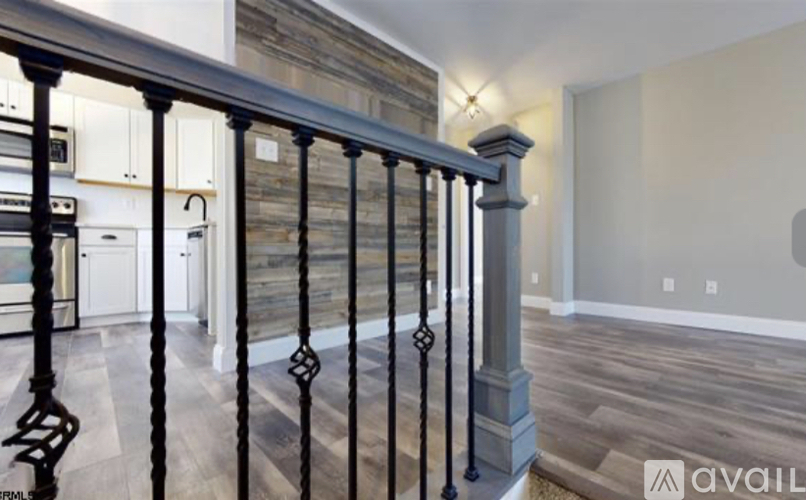 A black metal railing with a balustrade design is in the foreground of a modern kitchen and living room.