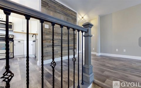 A black metal railing with a balustrade design is in the foreground of a modern kitchen and living room.
