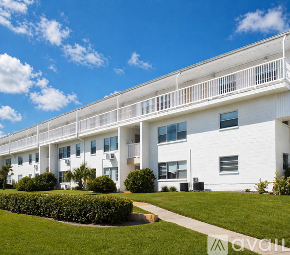 A white building with a balcony and a green lawn in front.