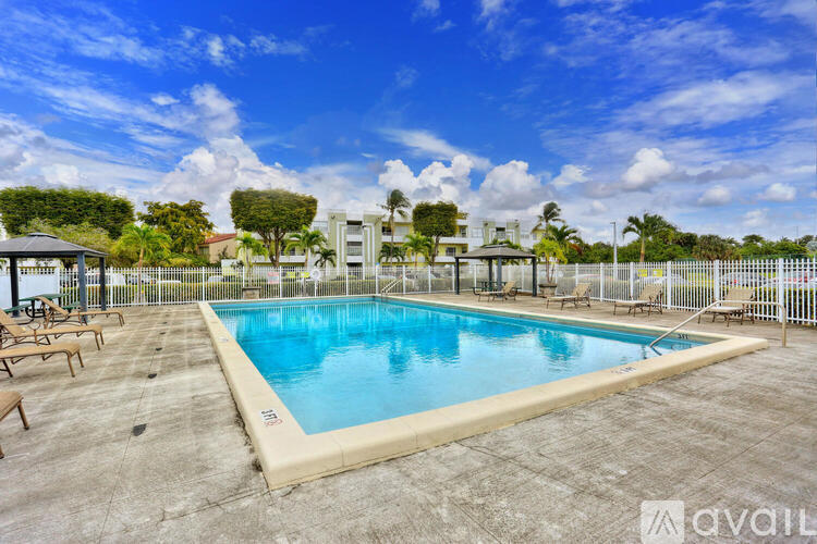 A large outdoor swimming pool surrounded by a fence and lounge chairs.