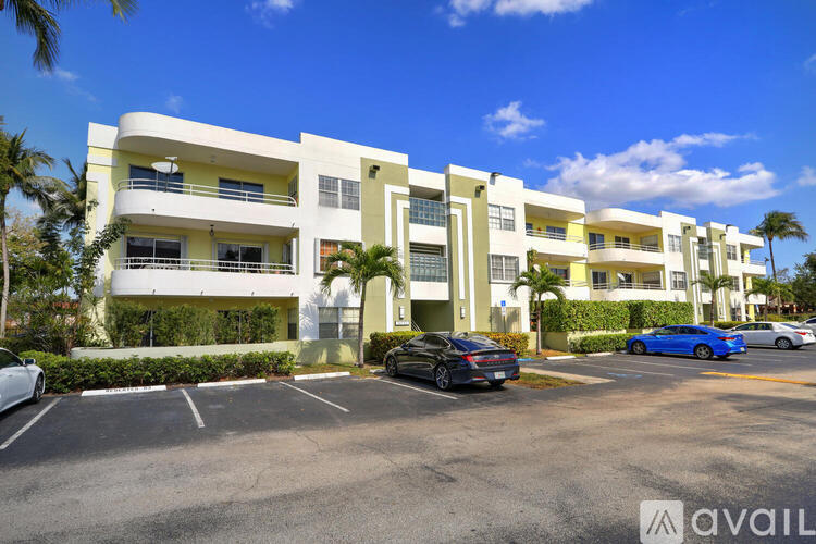A row of white apartment buildings with cars parked in front.
