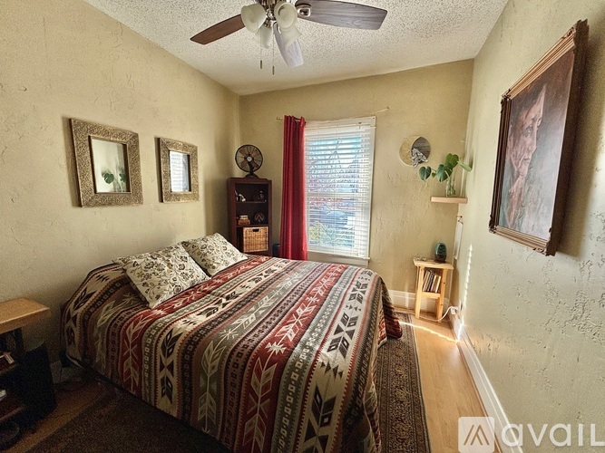 A bedroom with a bed, a ceiling fan, and a window with red curtains.