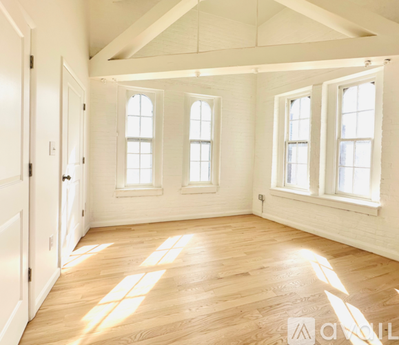 A room with wooden floors and white walls has three windows.