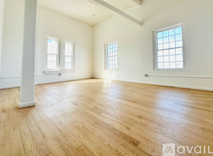 A spacious room with wooden flooring and three windows.