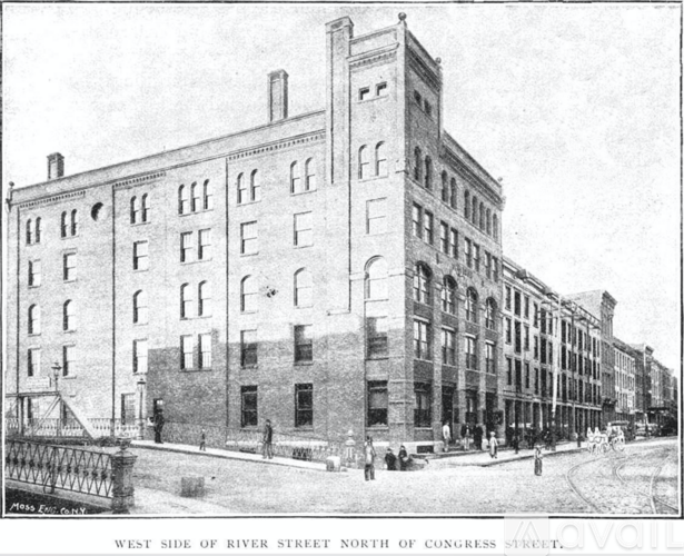 A black and white image of a street with a bridge and buildings.
