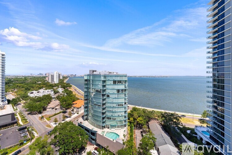 A tall glass building with a pool in the courtyard is surrounded by other buildings and the water.