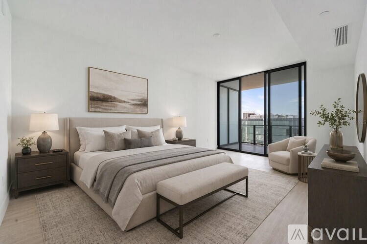 A bedroom with a large bed, a painting on the wall, and a view of the outside through the glass doors.