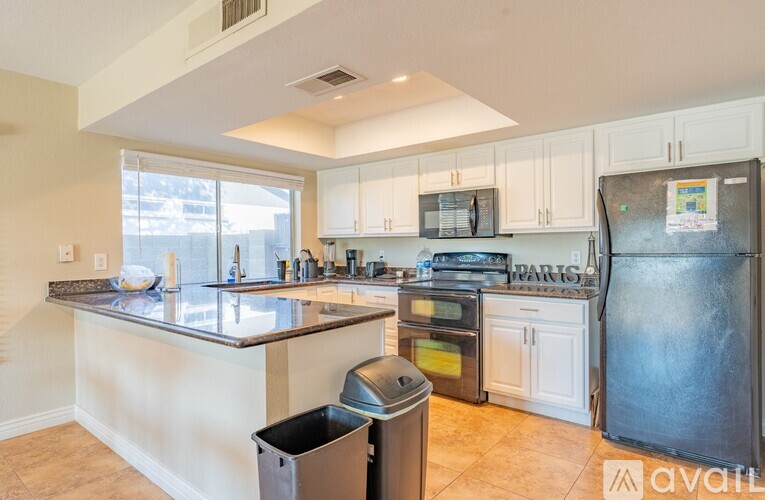 A kitchen with a black fridge and a black trash bin.