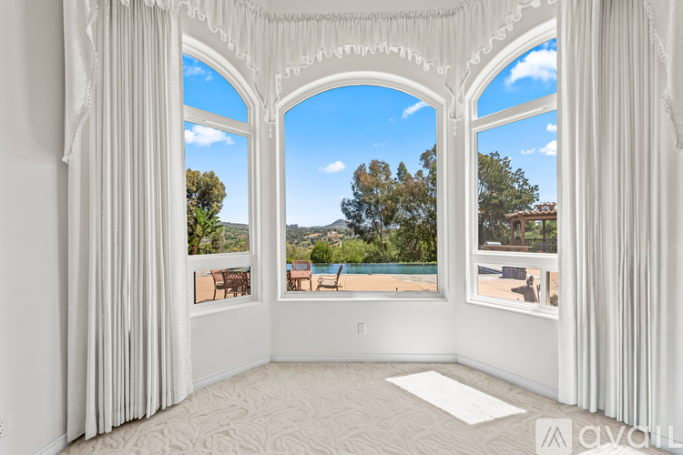 A room with white curtains and a large window overlooking a pool and trees.
