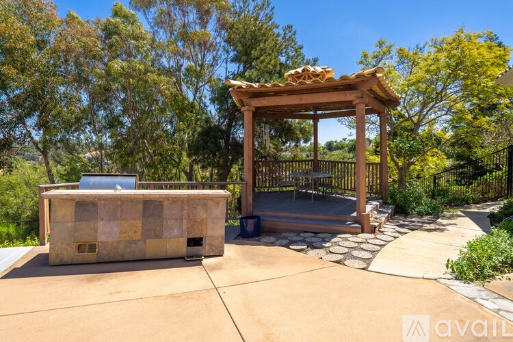 A gazebo with a stone bench is surrounded by trees.