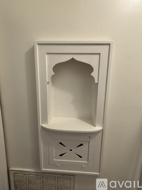 A white shelf with a decorative design on the front is mounted on a wall.