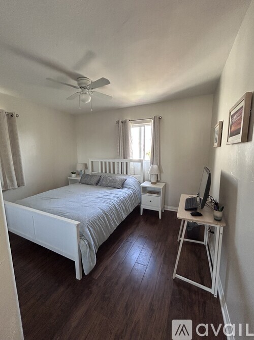 A bedroom with a bed, desk, and fan.