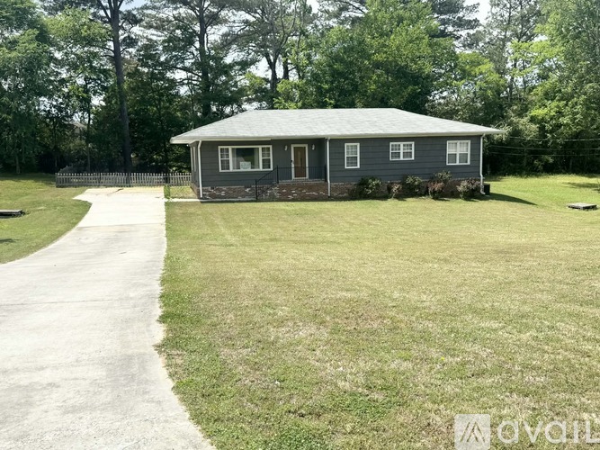 A house with a grey roof and a white fence is surrounded by a grassy area.