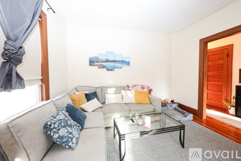 A living room with a grey couch, a glass coffee table, and a painting on the wall.