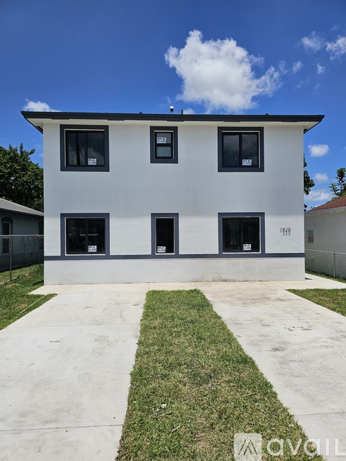 A white two-story house with a black fence and a green lawn in front.
