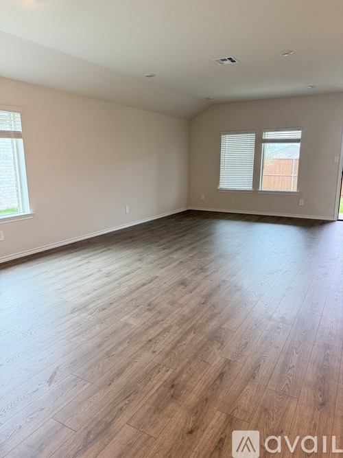 A spacious room with wooden flooring and two windows.