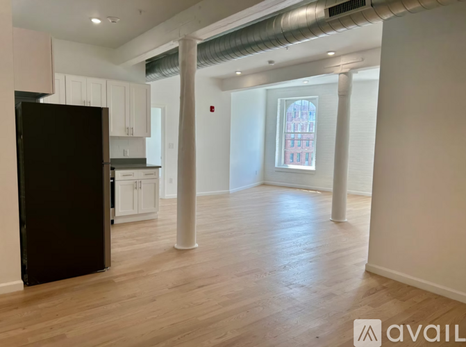 A black refrigerator is in a kitchen with white cabinets and a window.