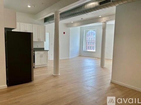 A black refrigerator is in a kitchen with white cabinets and a window.