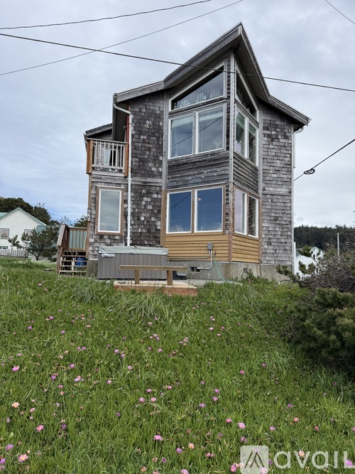 A house with a grey and brown exterior is surrounded by a field of flowers.