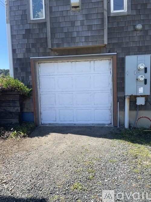 A white garage door is closed in front of a grey house.