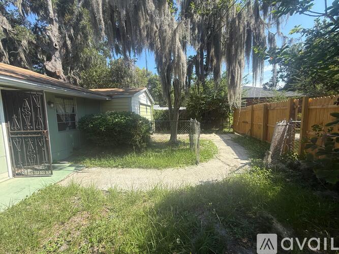 A house with a fence and a tree with Spanish moss hanging from it.