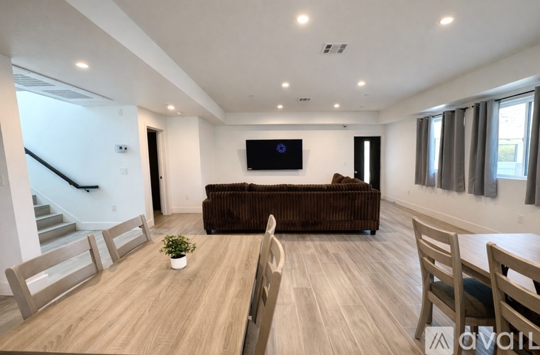 A living room with a brown couch, wooden chairs, and a flat screen TV mounted on the wall.