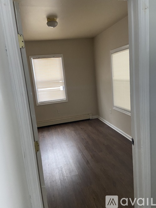 A room with wooden floors and two windows with blinds.