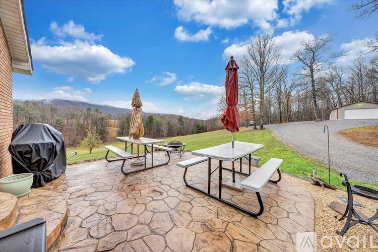 A patio with picnic tables and umbrellas is set against a backdrop of trees and a mountain.