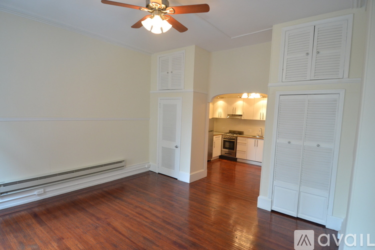 A room with a ceiling fan and a kitchen area in the background.