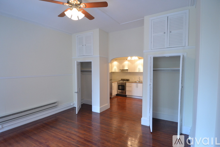 A room with a ceiling fan and a kitchen area in the background.
