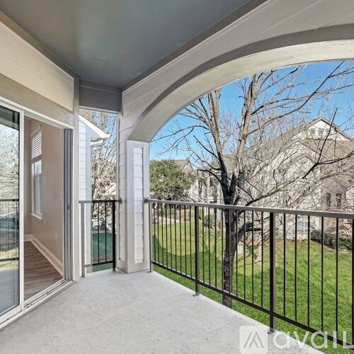 A balcony with a black railing and a view of a tree and a building.