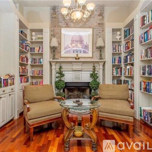 A living room with a fireplace, bookshelves, and a painting of a building.